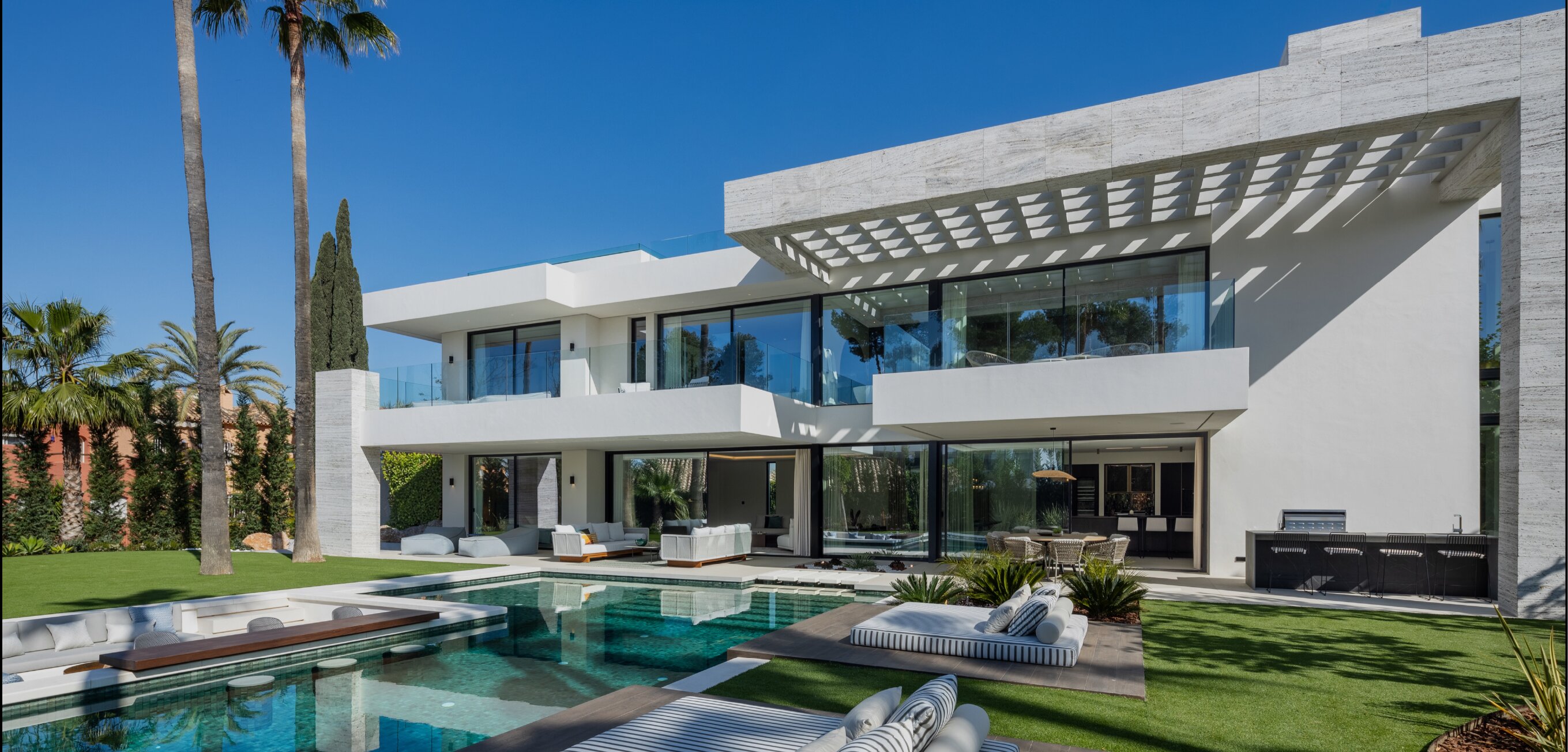 White luxury villa with swimming pool, palm trees and floor-to-ceiling windows.